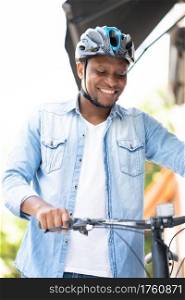 African American man wearing a helmet while walking with a bicycle on the street.