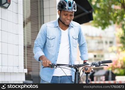 African American man wearing a helmet while walking with a bicycle on the street.