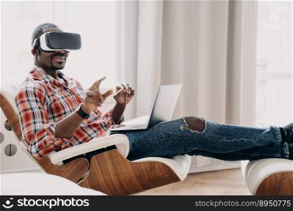 African american man wearing VR glasses making purchases in augmented reality store, play games. Modern black young guy working in cyberspace sitting in armchair with laptop. E commerce and tech. African american man in VR glasses making purchases in augmented reality store at laptop. E commerce
