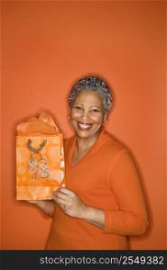 African American mature adult female holding gift bag smiling.
