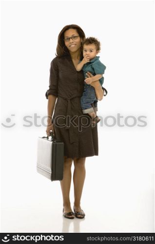 African American mid adult businesswoman holding toddler son on hip smiling at viewer.
