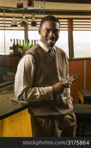 African American mid adult man at bar with martini smiling at viewer.