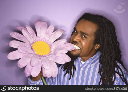 African-American mid-adult man biting big fake purple flower on purple background.