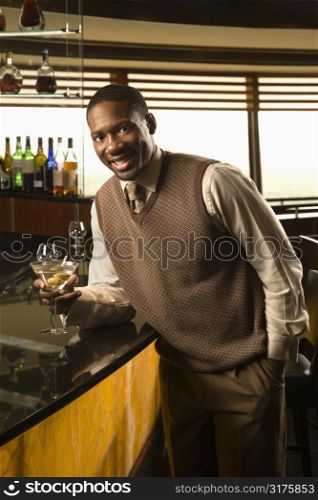 African American mid adult man leaning on bar with martini looking at viewer.