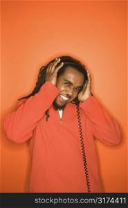 African-American mid-adult man listening to headphones wearing orange clothing on orange background.