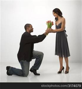 African American mid adult man on knees giving woman bouquet of flowers.