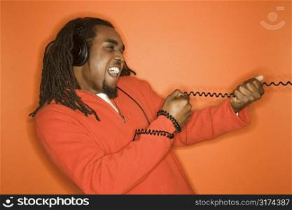 African-American mid-adult man pulling on cord wearing headphones and orange clothing on orange background.