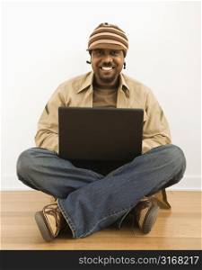 African-American mid-adult man sitting on floor smiling at viewer on laptop computer.