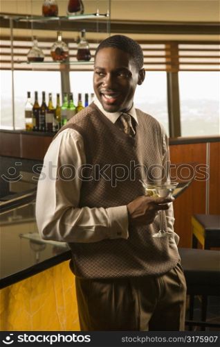 African American mid adult man standing at bar with martini.