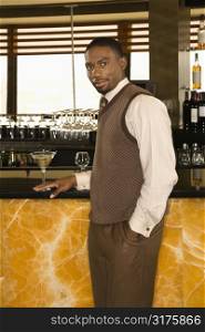 African American mid adult man standing at bar with martini looking at viewer.