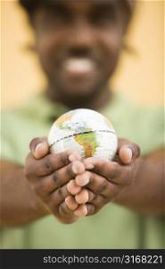 African-American mid-adult man wearing hat holding small globe toviewer.