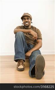 African-American mid-adult man wearing hat sitting on floor smiling at viewer.