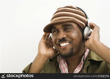 African-American mid-adult man wearing knit hat and listening to headphones smiling.