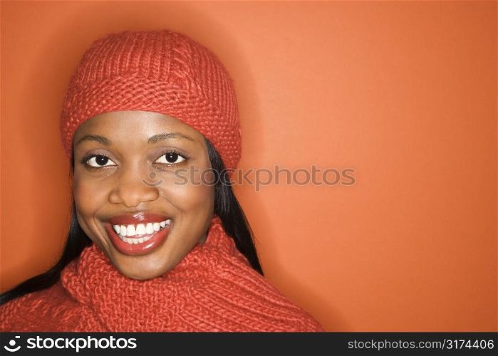 African-American mid-adult woman wearing orange scarf and hat on orange background.