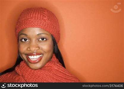 African-American mid-adult woman wearing orange scarf and hat on orange background.