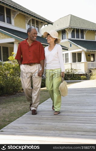 African American middle aged couple holding hands strolling on wooden walkway.