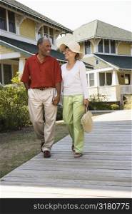 African American middle aged couple holding hands strolling on wooden walkway.