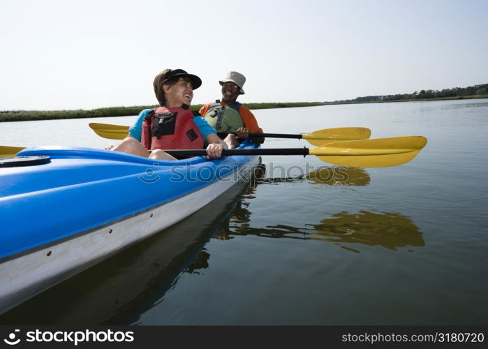African American middle-aged couple sitting in kayak on lake smiling and laughing.