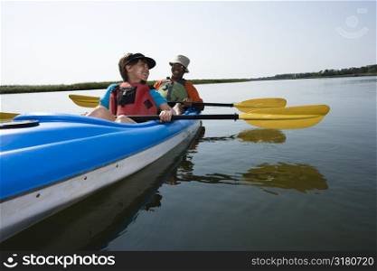African American middle-aged couple sitting in kayak on lake smiling and laughing.