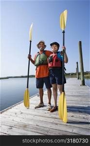 African American middle-aged couple standing on boat dock holding paddles and smiling at viewer.