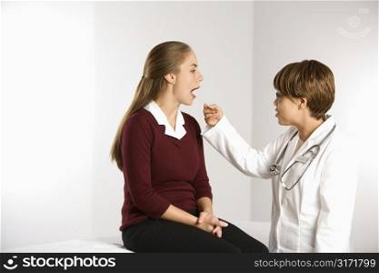 African American middle-aged female doctor examining Caucasian mid-adult female patient with tongue depressor.