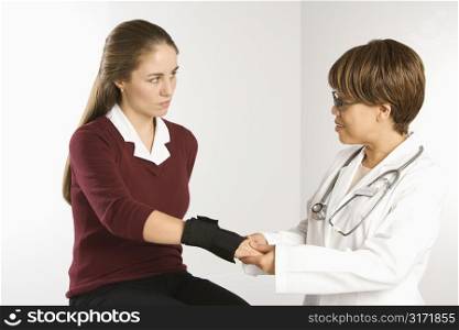 African American middle-aged female doctor examining wrist of Caucasian mid-adult female patient.