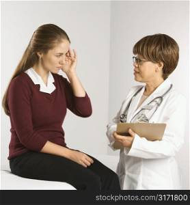 African American middle-aged female doctor listening to Caucasian mid-adult female patient explain her symptoms.