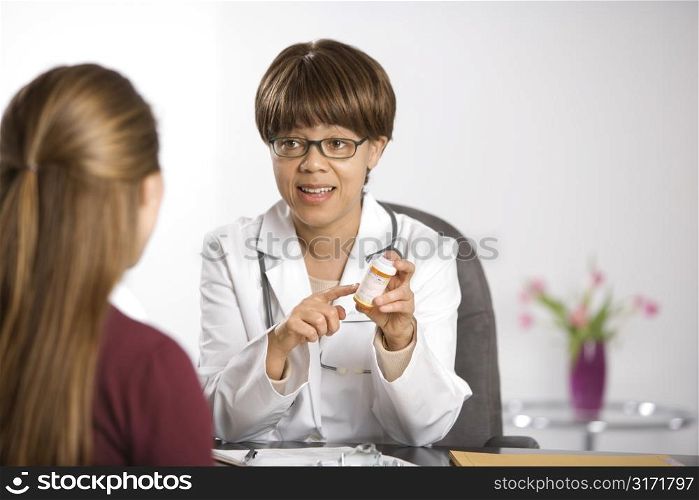 African American middle-aged female doctor sitting at desk explaining medication to Caucasian mid-adult female patient.