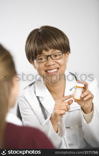 African American middle-aged female doctor sitting at desk explaining medication to Caucasian mid-adult female patient.
