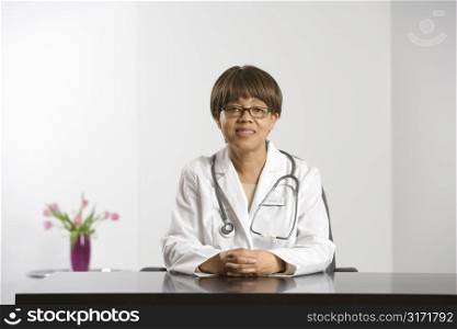 African American middle-aged female doctor sitting at desk smiling and looking at viewer.