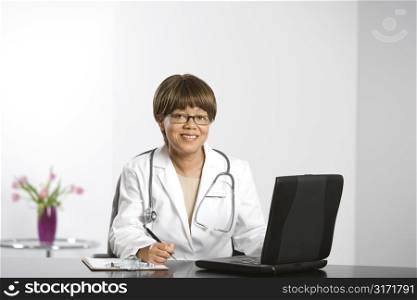 African American middle-aged female doctor sitting at desk working on laptop, smiling and looking at viewer.