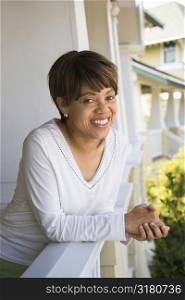 African American middle aged woman smiling at viewer and leaning on porch railing.