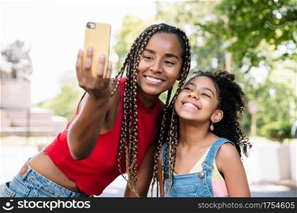 African american mother and daughter enjoying a day outdoors while taking a selfie with a mobile phone on the street.