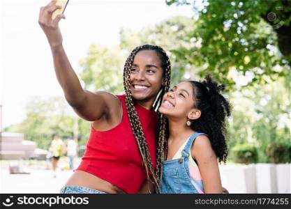 African american mother and daughter enjoying a day outdoors while taking a selfie with a mobile phone on the street.