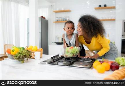 African American mother and son preparing salad together in the kitchen at home