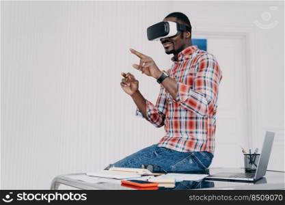African american student in vr glasses at home. Young businessman has remote virtual study. Afro freelancer is sitting on top of desk. Modern digital technology for business and e-learning.. African american student in vr glasses at home. Young businessman has remote virtual study.