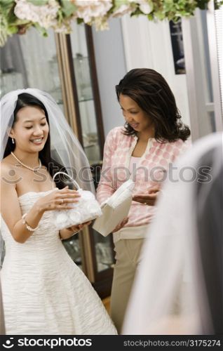 African-American woman helping Asian bride pick out handbag.