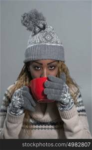African American woman in winter clothes enjoying a hot drink on gray background