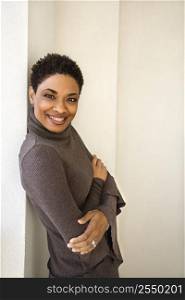 African-American woman standing leaning against wall smiling looking at viewer with arms crossed.