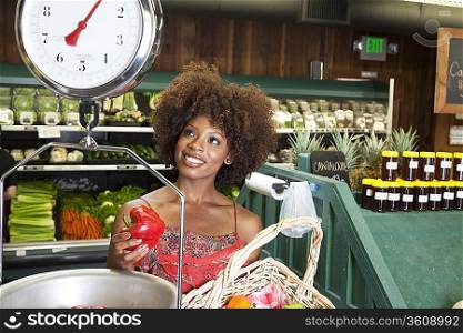 African American woman weighing bell peppers on scale at supermarket