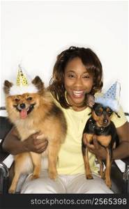 African American young adult female holding brown Pomeranian and Miniature Pinscher dogs wearing party hats.