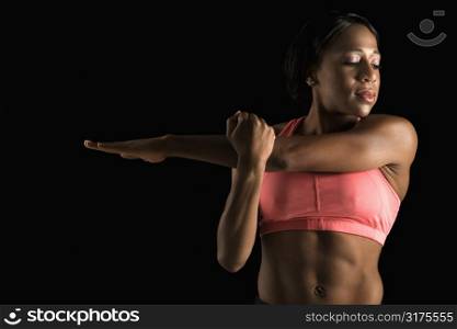 African American young adult woman in sports bra stretching arms with eyes closed.