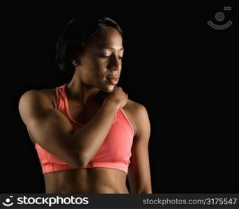 African American young adult woman in sports bra with hand on shoulder and eyes closed.