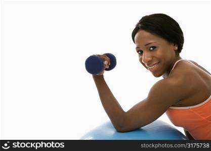 African American young adult woman leaning on exercise ball holding dumbbell and smiling at viewer.