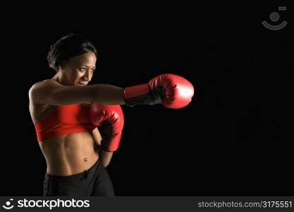 African American young adult woman wearing boxing gloves throwing punch.
