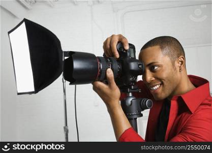 African American young male adult looking through camera on tripod.