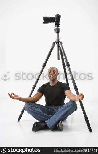 African American young male adult sitting meditating under camera and tripod.