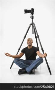African American young male adult sitting meditating under camera and tripod.