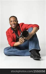 African American young male adult sitting on floor with camera looking at viewer smiling.