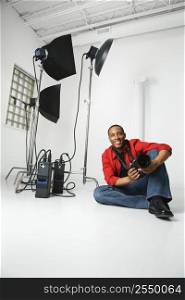 African American young male adult sitting on studio floor with camera.